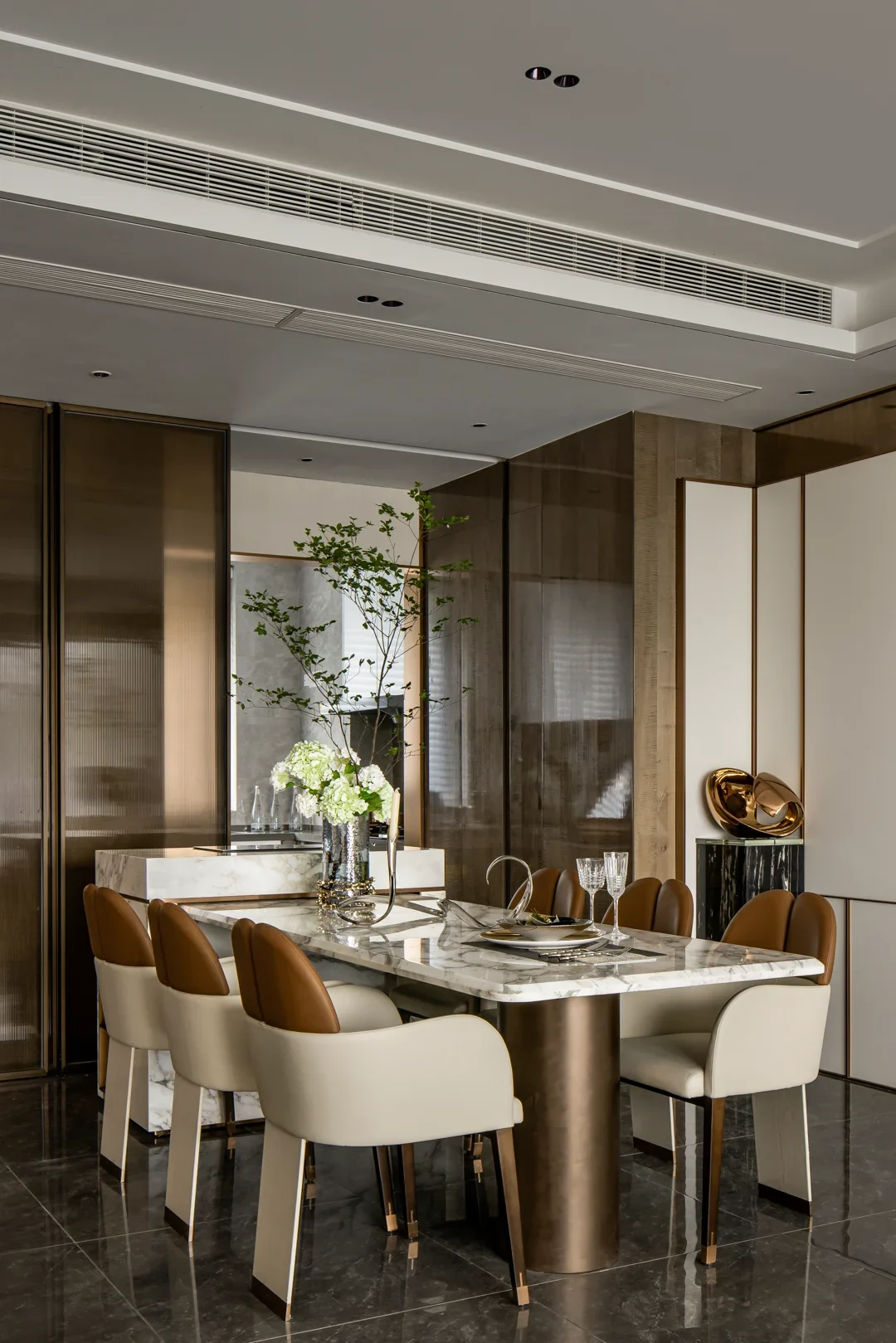 A stone dining table and upholstered chairs in a warmly lit contemporary dining room