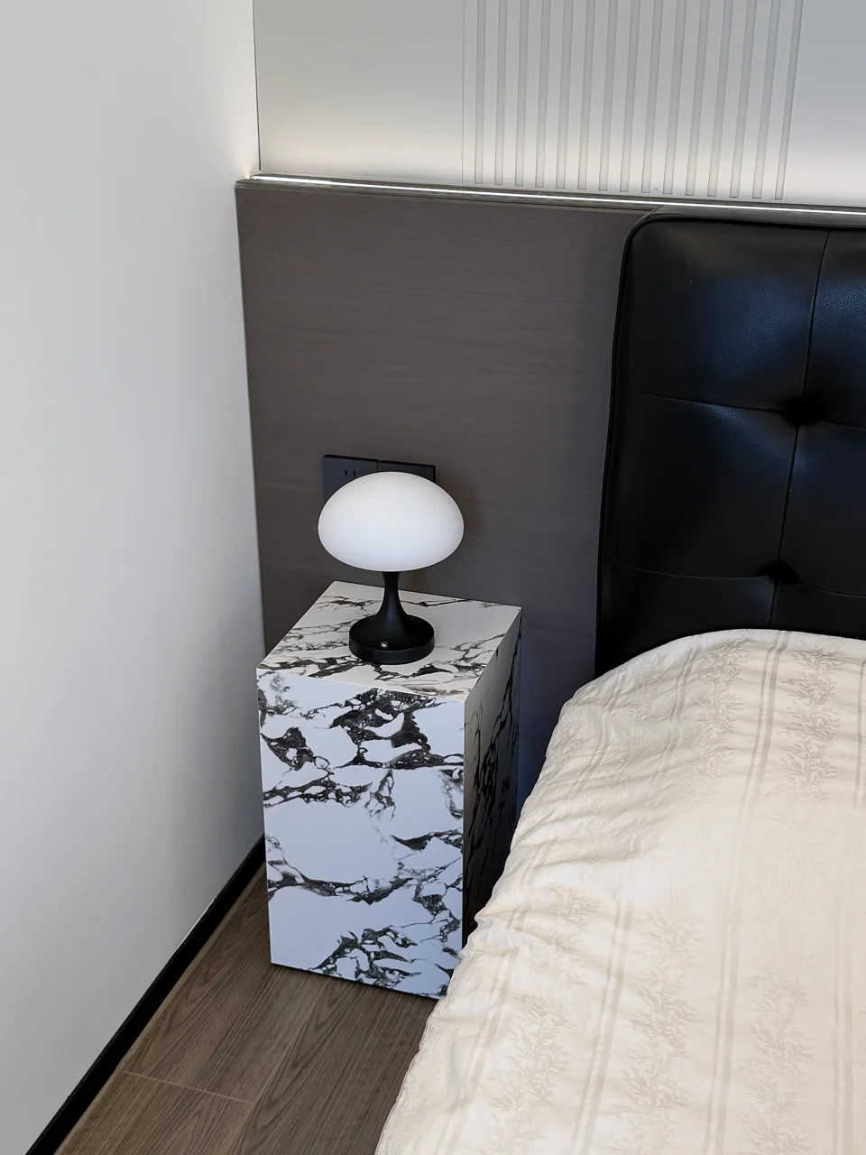 Compact black-and-white stone pedestal beside a bed